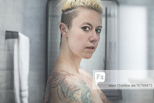 Portrait confident woman with tattoos and bare shoulders in bathroom