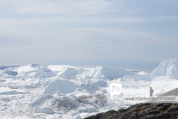 Mann steht auf einer Klippe mit Blick auf die Gletschereisschmelze in Grönland