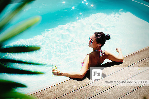 Frau entspannt mit Cocktail im sonnigen Sommer Schwimmbad