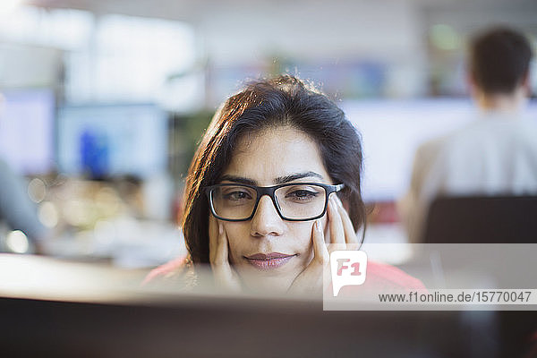 Konzentrierte Geschäftsfrau mit dem Kopf in den Händen  die im Büro am Computer arbeitet