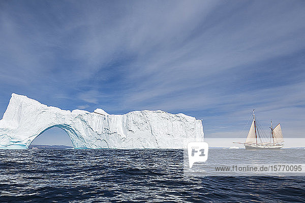 Schiff fährt auf sonnigen majestätischen Eisberg mit Bogen Grönland