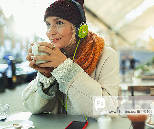 Junge Frau mit Kopfhörern hört Musik und trinkt Kaffee in einem Straßencafé