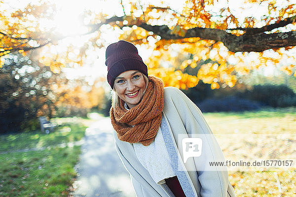 Portrait glückliche junge Frau in Strumpfmütze und Schal in sonnigem Herbstpark