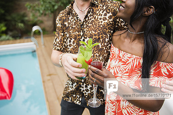Junges Paar trinkt Cocktails am Pool