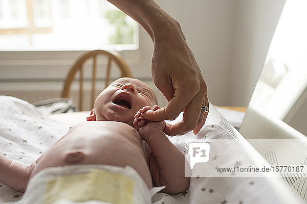 Mutter hält Hände mit weinendem neugeborenem Sohn auf dem Wickeltisch