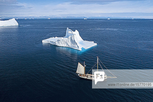 Schiff fährt an Eisberg vorbei auf sonnigem blauen Atlantik Grönland