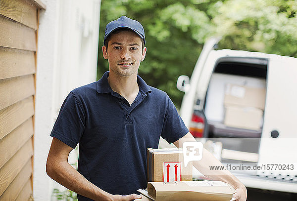 Porträt selbstbewusster Zusteller mit Paketen vor der Haustür