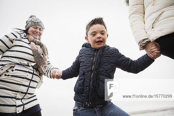 Porträt eines glücklichen  unbekümmerten Jungen mit Down-Syndrom  der mit seiner Mutter Händchen hält