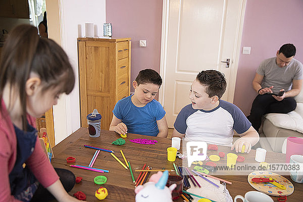 Junge mit Down-Syndrom und Geschwister spielen mit Spielzeug am Tisch