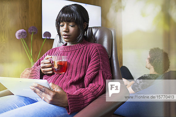 Junge Frau trinkt Tee und benutzt ein digitales Tablet