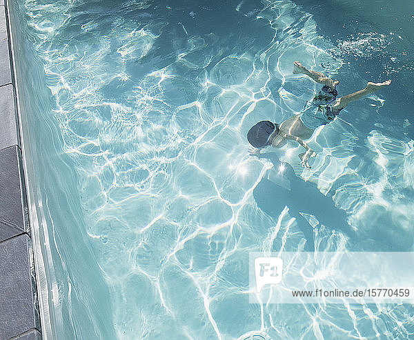 Junge schwimmt unter Wasser in einem sonnigen  sommerlichen Schwimmbad