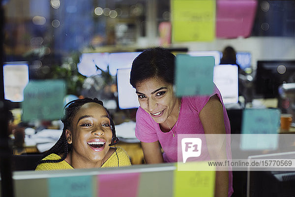 Glückliche Geschäftsfrauen mit Computer hinter Haftnotizen im Büro