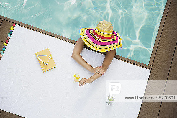 Frau mit Sonnenhut beim Auftragen von Sonnenschutzmittel im Schwimmbad