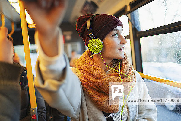 Junge Frau mit Strumpfmütze und Schal hört im Bus mit Kopfhörern Musik