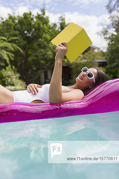 Woman relaxing reading book on inflatable raft in summer swimming pool
