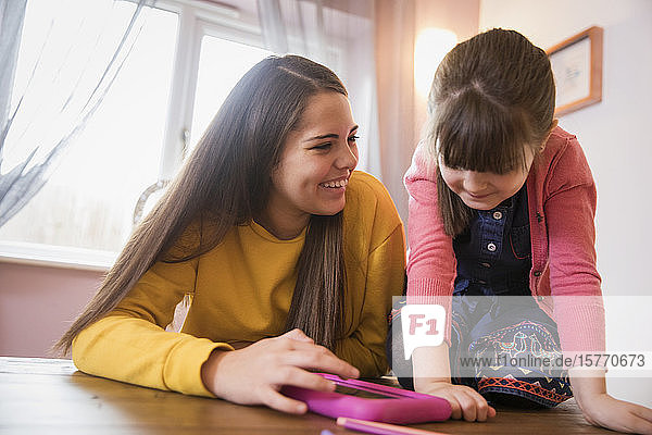 Fröhliche Schwestern mit digitalem Tablet am Tisch