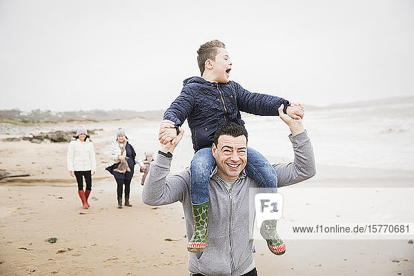 Glücklicher Vater trägt Sohn mit Down-Syndrom auf den Schultern am Strand