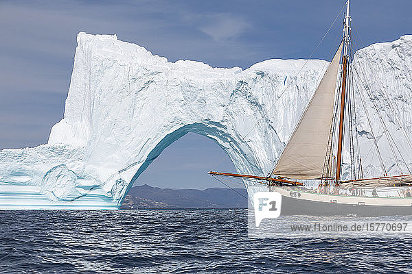Schiff fährt an sonnigem majestätischen Eisbergbogen auf dem grönländischen Ozean vorbei