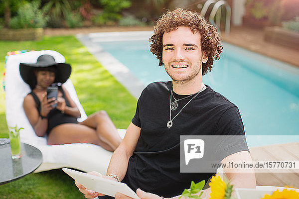 Porträt glücklicher junger Mann mit digitalem Tablet am Swimmingpool
