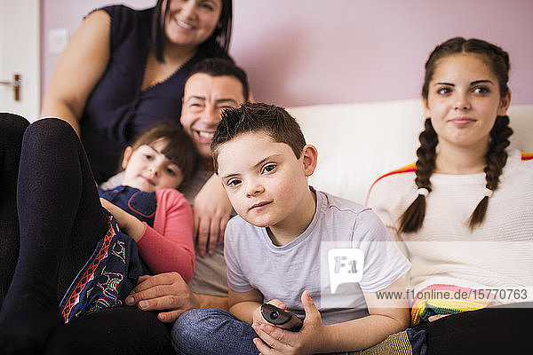 Porträt eines Jungen mit Down-Syndrom  der mit seiner Familie auf dem Sofa fernsieht