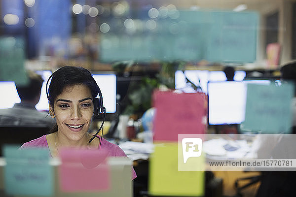 Businesswoman with headset working at computer in office behind adhesive notes