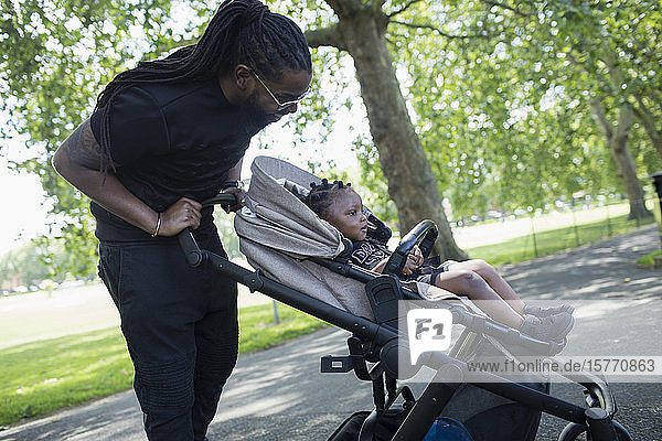 Vater schiebt Kleinkind im Kinderwagen in den Park
