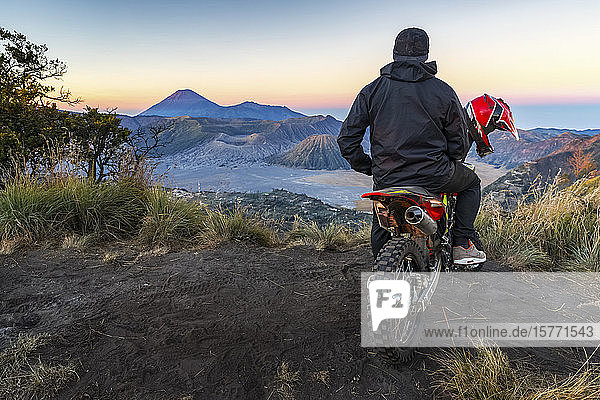 Ein Mann sitzt auf einem Motorrad und beobachtet den Sonnenaufgang am Bromo von einem geheimen Aussichtspunkt aus  Bromo Tengger Semeru National Park; Pasuruan  Ost-Java  Indonesien