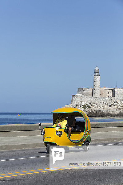 Yellow Cocotaxi on the Malecon Castillo del Morro (background); Havana Cuba
