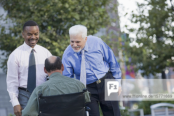 Two smiling businessmen and man on wheelchair outdoors