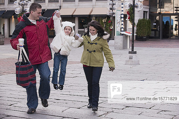 Mother and father walk with young daughter between them in a downtown shopping area