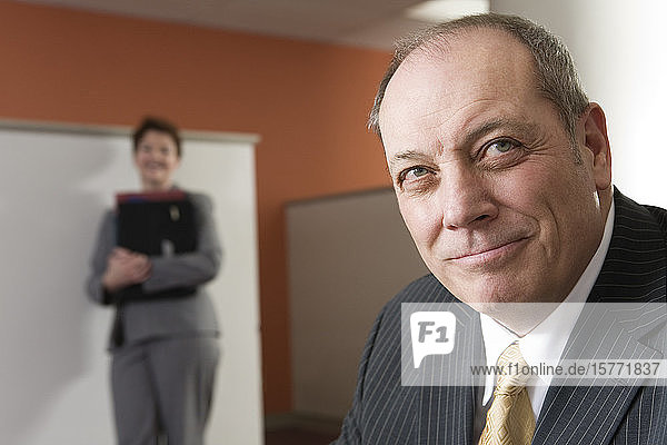 View of a business man smiling with business woman in background.