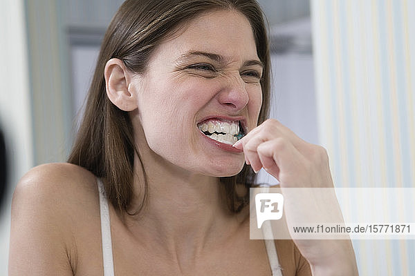 Eine junge Frau putzt sich vor dem Spiegel die Zähne.