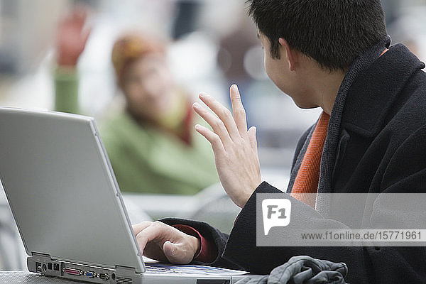 Seitenprofil eines jungen Mannes  der einen Laptop benutzt und mit der Hand winkt