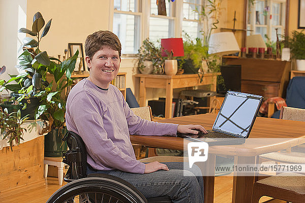 Behinderte Person im Rollstuhl  die zu Hause einen Laptop benutzt