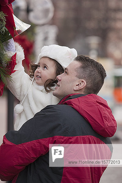 Zeit für den Vater und die kleine Tochter  während er sie im Arm hält und sie nach der Weihnachtsdekoration greift