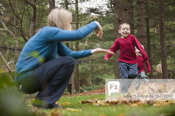 Mother signing to her son to jump in a pile of leaves as he runs in a park towards her
