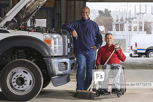 Fahrzeugmechaniker und Mann im Rollstuhl mit Besen posieren für ein Foto