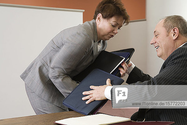 View of business man helping business woman hold files.