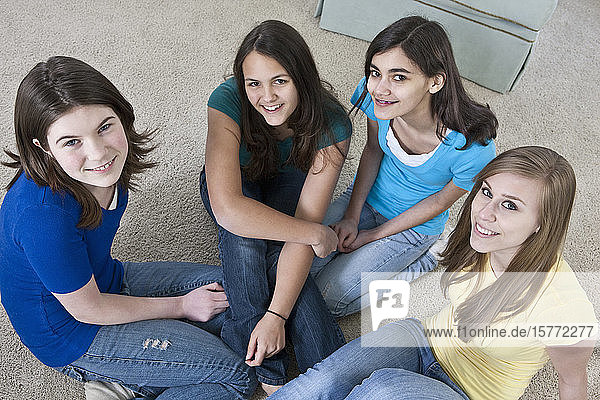 Portrait of four teenage girls sitting on the floor at home and looking up at the camera