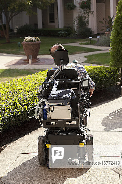 Tetraplegiker in einem Rollstuhl vor einem Haus