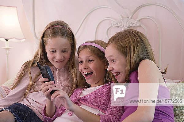 Blick auf drei süße Mädchen  die ein Handy halten.