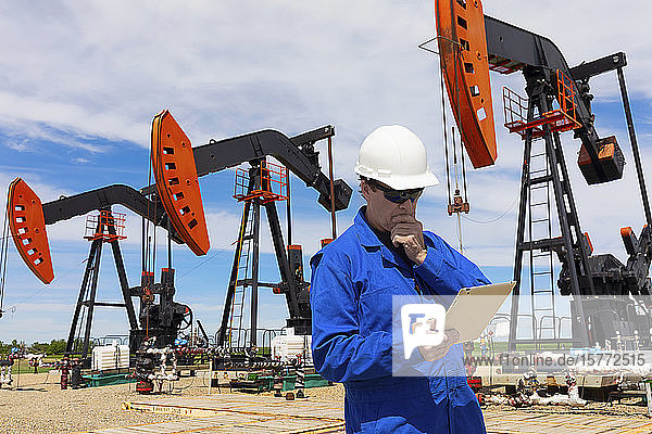 Man working on a tablet with pumpjacks in the background; Alberta  Canada