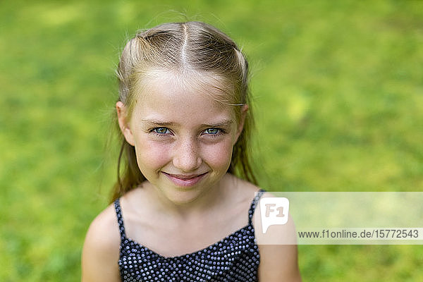 Porträt eines jungen Mädchens mit blondem Haar und blauen Augen  das in die Kamera blickt  mit leuchtend grünem Gras als Hintergrund; British Columbia  Kanada