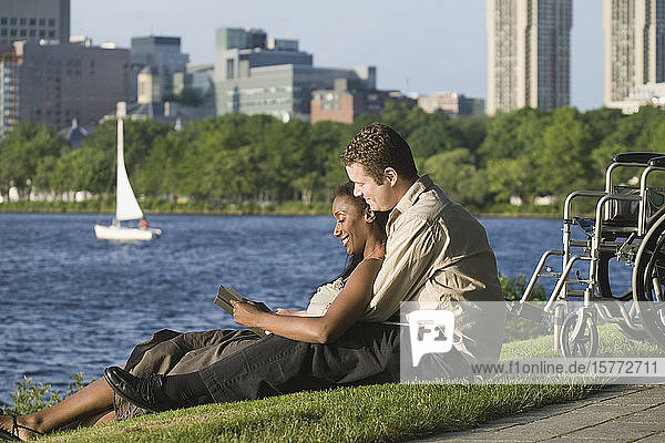 Seitenprofil eines Paares im mittleren Erwachsenenalter  das in einem Park sitzt und ein Buch liest.