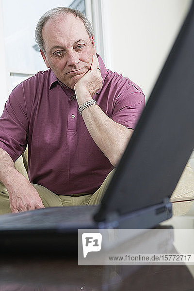 Blick auf einen verwirrten Mann  der auf einen Laptop schaut.