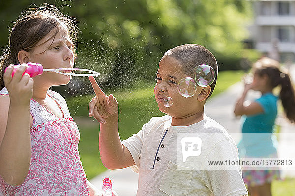 Ein Mädchen bläst Seifenblasen und ein Junge berührt den Seifenblasenstab