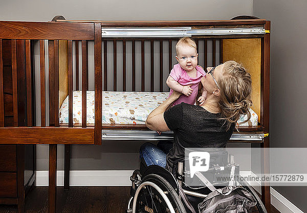 Eine querschnittsgelähmte Mutter hebt ihr Baby aus einem speziell angefertigten  seitlich zu öffnenden Bettchen  das es ihr ermöglicht  ihr Baby vom Rollstuhl aus zum Schlafen hinzulegen: Edmonton  Alberta  Kanada