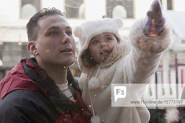 Zeit für den Vater und die kleine Tochter  während er sie im Arm hält und sie auf etwas in einem Fenster zeigt