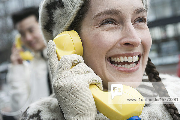 Nahaufnahme einer jungen Frau  die lächelnd in ein Münztelefon spricht