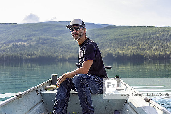 Mann sitzt in einem kleinen Ruderboot mit Motor auf dem White Lake mit dem ruhigen Wasser  in dem sich der Wald im Hintergrund spiegelt; British Columbia  Kanada